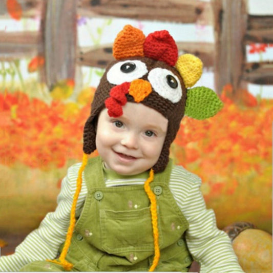 Thanksgiving hand-woven turkey hat worn by a smiling child in a green outfit with fall background.
